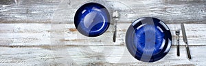 Basic dinner table setting of an empty main dark blue dish and bowl with cutlery on white wood