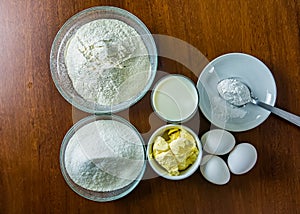 Basic ingredients for making cake, flour, sugar, milk, eggs, butter and yeast on wooden table. Ingredients for homemade cake