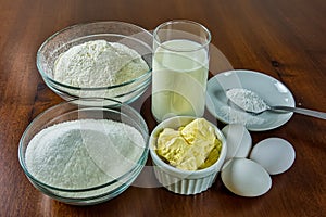 Basic ingredients for making cake, flour, sugar, milk, eggs, butter and yeast on wooden table. Ingredients for homemade cake