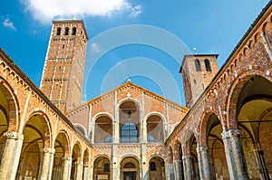 Basilica of Sant`Ambrogio church brick building with bell towers, courtyard, arches, blue sky background, Milan