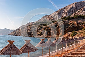 Baska - Straw umbrellas and loungers on idyllic pebble beach in resort town Baska, Krk Otok, Primorje-Gorski Kotar, Croatia