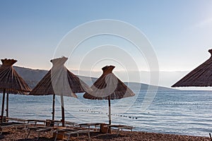 Baska - Straw umbrellas and loungers on idyllic pebble beach in resort town Baska, Krk Otok, Primorje-Gorski Kotar, Croatia