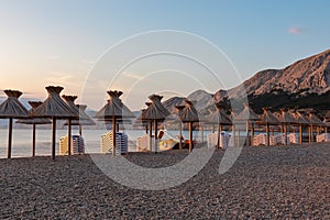 Baska - Straw umbrellas and loungers on idyllic pebble beach in resort town Baska, Krk Otok, Primorje-Gorski Kotar, Croatia