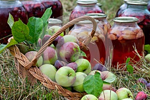 Basket of apples in the grass. Jars with fruit compote on the background. Concept of preserving fruit for the winter
