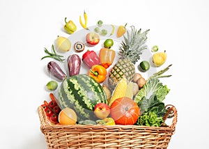 Basket with assortment of fresh organic fruits and vegetables on white background, top view