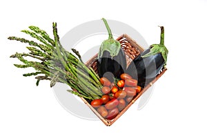 Basket with bunch of asparagus, tomato and aubergines isolated