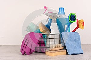 Basket with cleaning products against light wall background with copy space