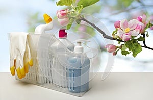 Basket of cleaning products, rubber gloves on the table on blurry spring background with apple blossoms Cleaning concept