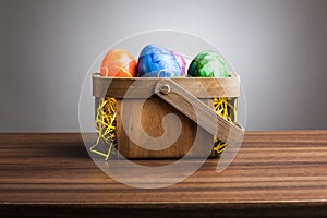 Basket, colored easter eggs on table, gray background