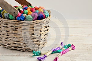 Basket with colored threads of floss on white wooden background.