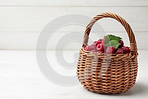 Basket of delicious fresh ripe raspberries with leaves on white wooden table