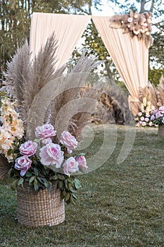 A basket with dried pampas leaves and pastel pink roses. Decor for an aisle of a rustic garden wedding ceremony
