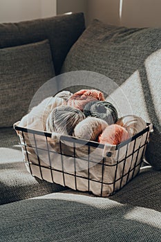 Basket of earth coloured skeins of yarn on a sofa, cool tones, selective focus