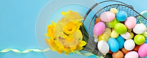 Basket with Easter eggs and bouquet of yellow narcissus on blue paper background. Flat lay  top view with copy space. Banner for