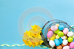 Basket with Easter eggs and bouquet of yellow narcissus on blue paper background. Flat lay  top view with copy space. Banner for