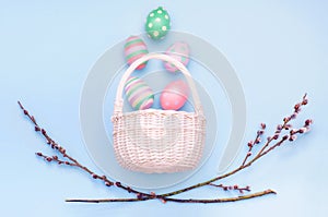 basket with Easter eggs and branches of flowering willow on a blue background