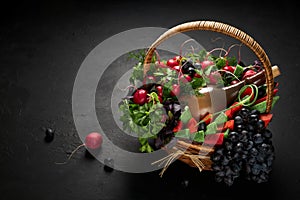 Basket filled with vegetables, cheese, grapes and a bottle of wine on a black background