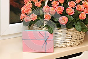 Basket of flowers, a bouquet of roses with a gift is on the windowsill