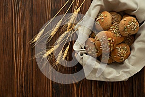 Basket of fresh homemade crispy bread buns with bran, sunflower and pumpkin seeds on brown wooden background. Top view