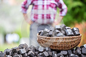 Basket full of coal briquettes on a pile with a man standing in background with arms on his waist