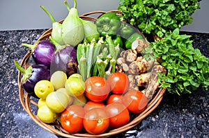 Basket full of different varieties of vegetables tomato lemon eggplant gourd taro ladyfinger bell pepper mint coriander.