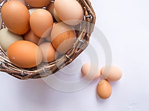 Basket full of eggs on a white table with three eggs outside the basket. Top view.