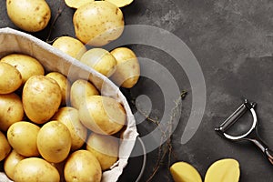 Basket full of fresh, young potatoes board, towel and knife on gray background