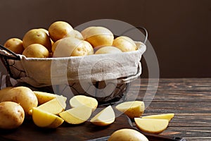 Basket full of fresh, young potatoes board, towel and knife on wooden background