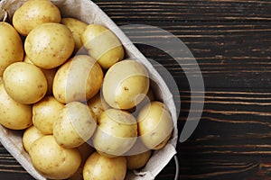 Basket full of fresh, young potatoes board, towel and knife on wooden background