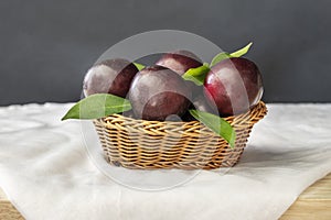 A basket full of ripe red plums with green leaves along