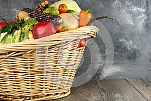 Basket full of vegetables and fruits stands on the floor against a gray wall. Autumn and harvest time. Space for text