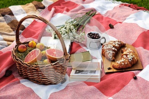 Basket with grapefruit and apricots, a glass with a cherry, a bouquet of white flowers, two croissants on a wooden board, books.