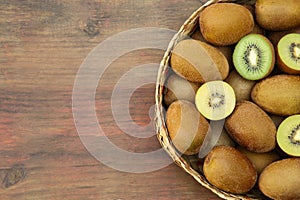 Basket of many whole and cut fresh kiwis on wooden table, top view. Space for text