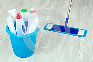 Basket and mop with variety cleaning products on wooden floor. Cleaning concept