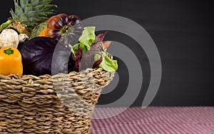 BASKET OF ORGANIC FRESH VEGETABLES AND FRUITS FROM FARMERS MARKET ON TABLE WITH RED CHECKERED FABRIC