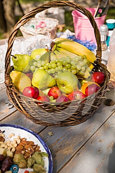 Basket with organic fruit apples, pears, bananas and grapes on the wooden table with nuts and other ingridients