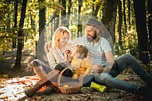 Basket with picnic meal and toys for the kid. Happy family of three lying in the grass in autumn. The concept of a happy