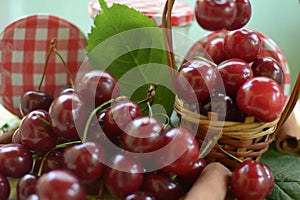 Basket with red cherries with stems and jar with cherries on yellow tablecloth