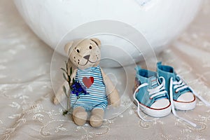 Basket shell of Easter eggs, flat shoes baby boy and a teddy bear with a heart close-up, requisites for a photo session of a newbo