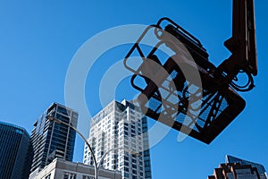 Basket for skylift against blue sky and city architecture. Hydraulic lifting platform at construction site