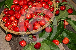 Basket of sweet and ripe cherries with leaves on wooden background photo