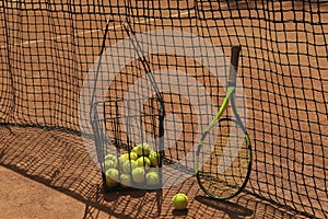 Basket tennis balls and racket against net on clay court