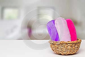 Basket with three colorful terry towels or cosmetic for body care on a white table over blurred bath background with copy space.