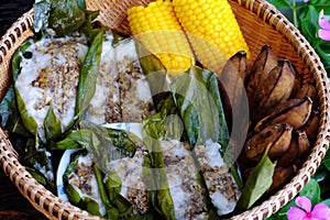 Basket of Vietnamese homemade food, boiled yellow corn, steam banana and vegan rice cake that wrap by leaf