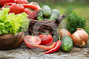 Basket and wooden plate with fresh vegetables (tomatoes, cucumber, chili pepers, dill and lettuce) on wooden background.