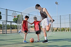 Basketball coach doing leg stretching exercises with two children, one of them has a leg prosthesis