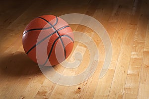 Basketball on hardwood court floor with spot lighting