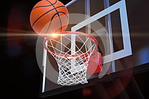 Basketball heading to the net at a sports arena with lens flare .