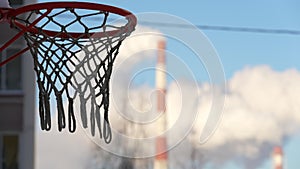 A basketball hoop against the background of the smoking chimney of a thermal power plant in winter. Selective focus