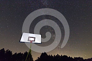 Basketball hoop and board under starry night. Milky way galaxy. Basketball court in night sky.